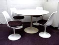  Ronde tafel hoog 73 cm met 4 stoelen hoog 80 cm model Tulip ontwerp Eero Saarinen 1959 uitvoering Arkana Engeland op latere datum Stoelen Wit gelakt kunststof frame op aluminium poot losse grijze stoffen zitkussens Tafel Wit gelamineerd blad en gegoten aluminium poot 