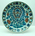 Schotel met symetrische decoratie van bloemen en op de rand een band met bloemmotieven oud-Perzisch in rood blauw en groen op een wit fond uitvoering de Porceleyne Fles 1910-1949 