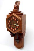 Houten Amsterdamse School wandklok opgebouwd uit veschillende houtsoorten ingekleurde eternieten wijzerplaat en metalen slinger met houten handgeneden beeldje van een haan op bovenzijde Nederland ca.1920 