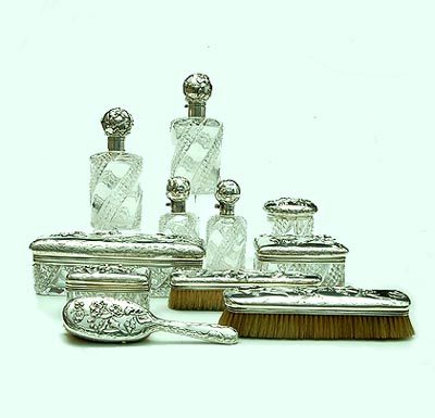 An Art Nouveau silver cut crystal toilet garniture chased and hammered silver each object with a different flower or plant mounted on crystal cut with geometrical patterns consisting of four flasks with hinged covers and glass stoppers four boxes and covers and three brushes design Phillipe Wolfers executed by Wolfers Frères Belgium / Brussels ca.1900 