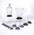 Delen van het water- sherrystel Palu karaf met stop schenkkan en 10 bekerglazen in drie maten hoog 5,8 / 9,7 11,2 cm met een blauwpaarse in 10 facetten geslepen voet ontwerp A.D.Copier 1938 uitvoering Glasfabriek Leerdam 